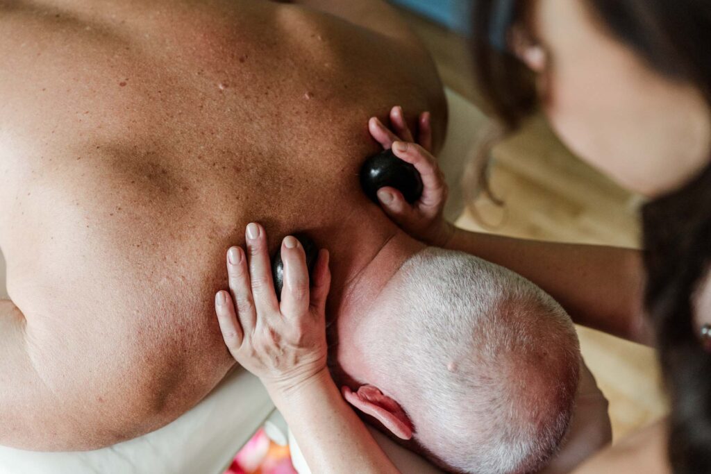 Dieses Bild zeigt eine Nahaufnahme von Sonja Blessing während sie eine ʻIli ʻIli H﻿ot Stone Massage ausübt und warme Steine auf den Schultern des Kunden platziert.